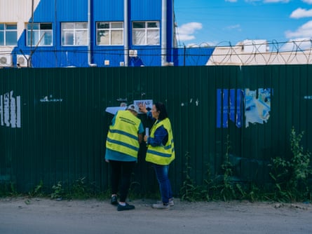 Workers in hi-vis put up posters on a wall