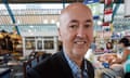 Geraint Davies inside Swansea indoor market; he wears a dark jacket with open-necked blue and white checked shirt; he is bald, with black eyebrows