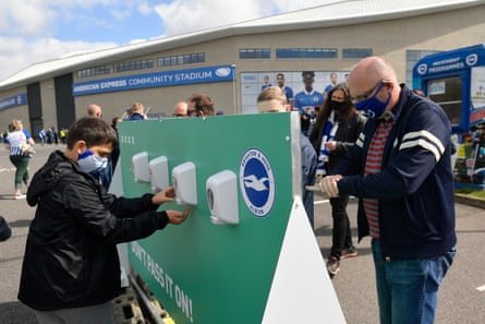 Fans wearing masks use one of a number of hand sanitiser stations outside the stadium.