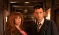 Actors Catherine Tate and David Tennant standing looking tense in a magical wooden corridor.