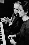 The composer Malcolm Williamson with Thea Musgrave in London in April 1965. They are seated at a piano and Williamson is pointing and gesturing while Musgrave reads the music.