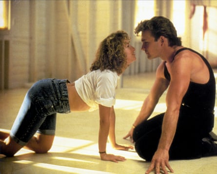 A woman in long jeans shorts, her shirt pulled above her stomach, is on all fours across from a kneeling man, their noses almost touching