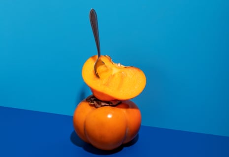 Fuyu Persimmons  with spoon on a blue background.