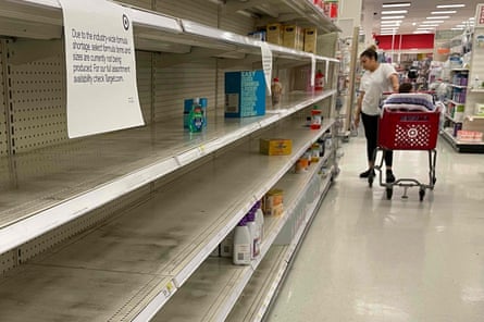 A woman with a baby sitting in her cart looks at empty shelves at a Target store. A sign over the shelves reads, ‘Due to the industry-wide formula shortage, select formula items and sizes are currently not being produced. For our full assortment availability, check Target.com.’