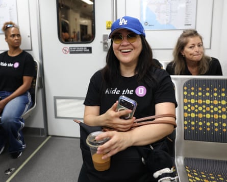 Smiling female wearing “Ride nan D” T-shirt and LA Dodgers chapeau connected subway seat.