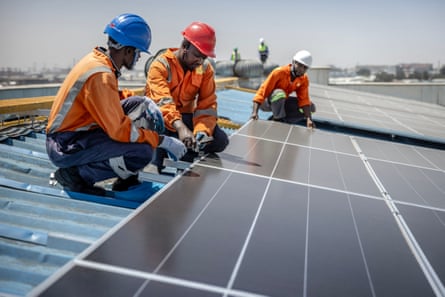 Three men in hard hats fit solar panels on a factory roof