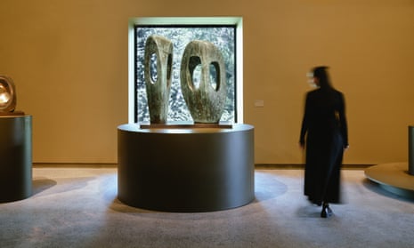 A woman inspects two sculptures. The works are upright, elegantly curved, and a mottled green colour with large holes in them allowing the viewer to see the garden behind