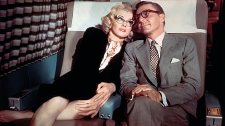 Marilyn Monroe sitting on a seat sit next to a man, in a black skirt and jacket.