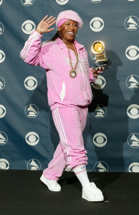 Missy Elliot dressed in a pink velour Adidas tracksuit and a pink cap on top of a pink bandana and holding a grammy award
