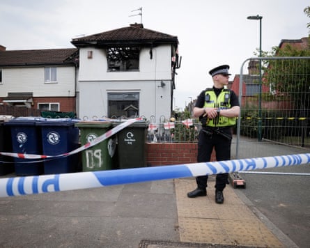 A police officer stands outside a burned-out house cordoned off by police tape