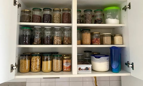 kitchen cabinet stocked with jars of beans, pasta, rice and flour etc