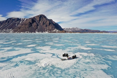 Two men working near snowmobiles on ice where the sea has frozen