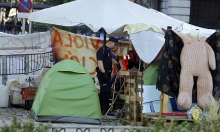 A police officer searches a makeshift shelter used by homeless protesters outside the health ministry in Madrid