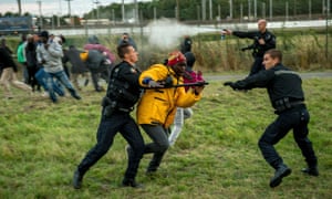 French gendarmes try to stop migrants near the Eurotunnel in Coquelles, near Calais