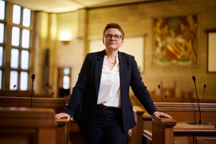 Bev Craig, Manchester council leader, stands between wooden benches in a council chamber