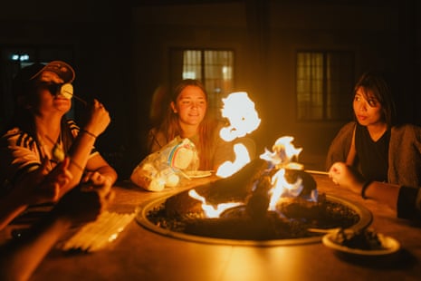 Young women sit around a bonfire