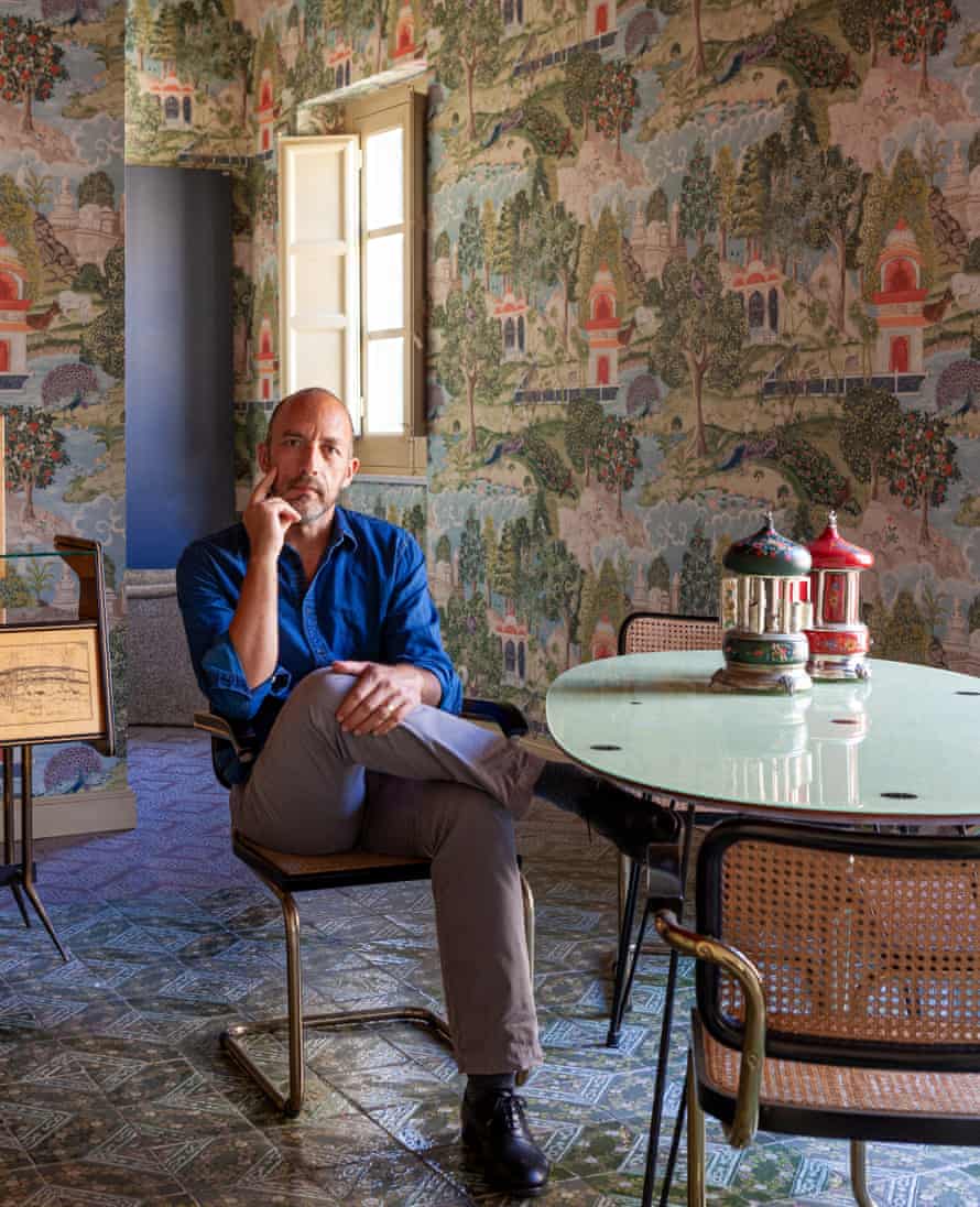 Owner Dario Longo seated at a modern table with a wall of frescoes behind him