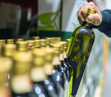 A closeup shot of a man buying olive oil at a supermarket. He is taking a bottle of olive oil from the shelf.