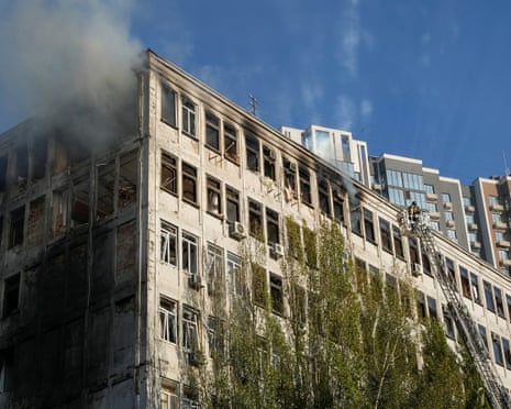A firefighter on a ladder platform tackles smoke from a building damaged in a drone strike