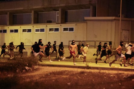 A group of young men, some wearing balaclavas and masks, run along a pavement at night.
