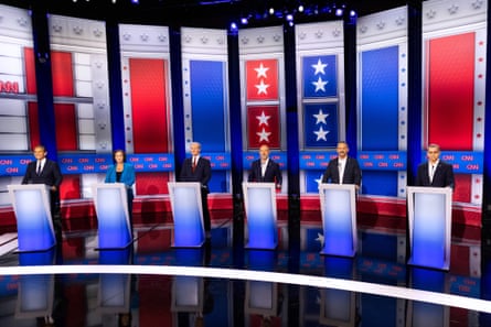 From left to right, Antonio Villaraigosa, Katie Porter, Tom Steyer, Steve Hilton, Chad Bianco and Xavier Becerra stand before podiums on a dark stage before a backdrop of red, white and blue banners.