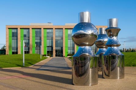 A highly reflective silvery metal sculpture of three curved, cylindrical forms