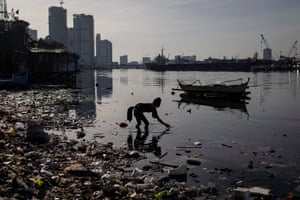 A woman picks a water bottle from washed-up rubbish in river