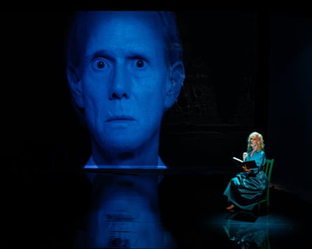 Kit Green playing a tortured looking woman on a big screen and a relaxed woman on stage