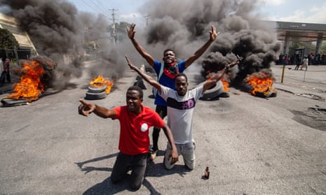 Protesters set fire to tyres in a road in Port-au-Prince, Haiti, 12 March 2024: three men, two kneeling and one standing, hold their arms out and shout as black smoke billows from piles of tyres behind them