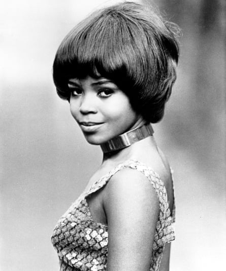 Wearing a sequinned strappy top, she stands at a right angle to the camera, head turned towards it