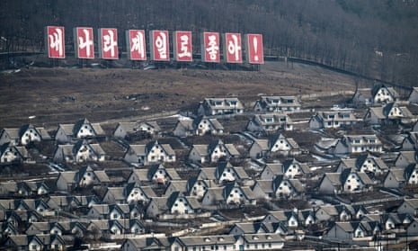 A drab settlement with a Korean-language sign on the hillside in white lettering on a red backdrop
