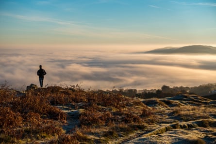 A woman stands on the top of a moor with clouds below