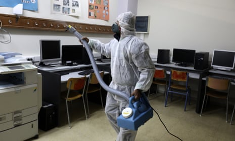 A worker wearing a protective suit sprays disinfectant inside a classroom at a high school in Athens.