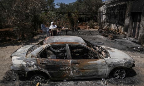 a woman stands behind burnt car outside