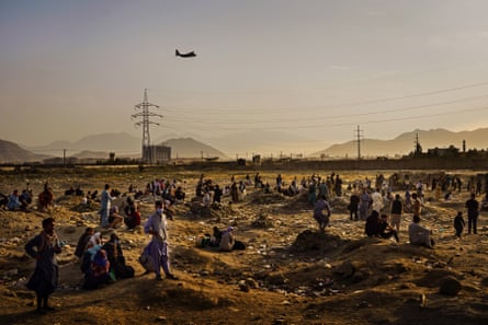 A military transport plane departs overhead as Afghans hoping to leave the country wait outside the Kabul airport in August 2021