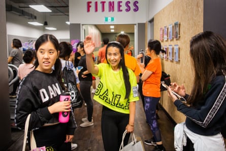 A middle-aged Asian woman wearing a neon yellow T-shirt waves at her friends.