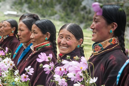 A row of women in traditional dress and jewellery hold pink flowers.