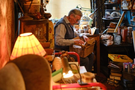 Michael Palin looking through papers in a basket, in a room packed with objects and books