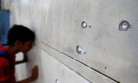 A boy peers through bullet holes after a gunfight outside a a supermarket in one of Caracas’s poorer neighbourhoods.