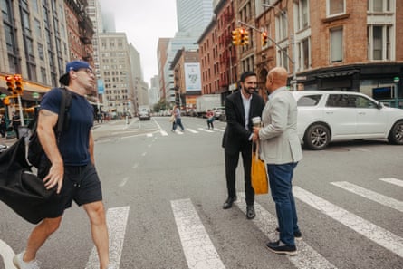 Zohran Mamdani smiles and shakes hands with a man standing on a pedestrian crossing on a Manhattan street