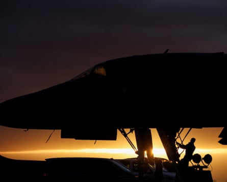 An engineer working on the forward landing gear of an aircraft is silhouetted against the setting sun