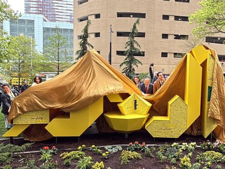 A gold cloth being pulled off a yellow monument in the shape of the Arabic word for âÂÂthe penâÂÂ