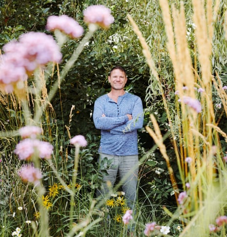 Steve Backshall standing in the midst of tree branches and wild flowers