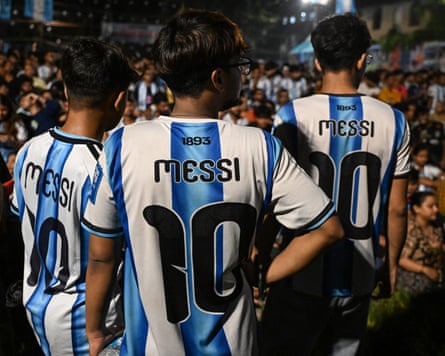 Three Indian men wearing Lionel Messi 10 Argentina shirts watch the 2026 World Cup final in a fanzone in Kolkata.