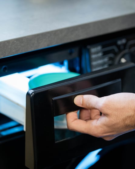 A hand opening the washing powder drawer of a washing machine