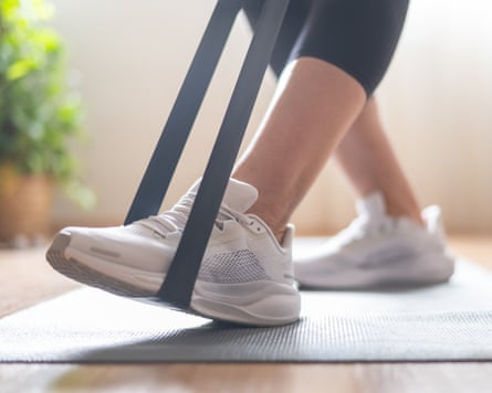 A woman standing on a yoga mat, using a black resistance band for a leg workout.