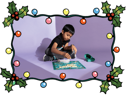 A photograph of a boy playing Scrabble inside a holly and Christmas lights frame