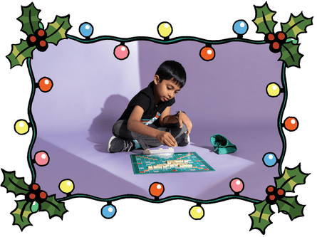 Une photographie d'un garçon jouant au Scrabble à l'intérieur d'un cadre de houx et de lumières de Noël