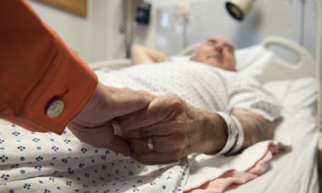Elderly man in hospital bed, holding someone's hand