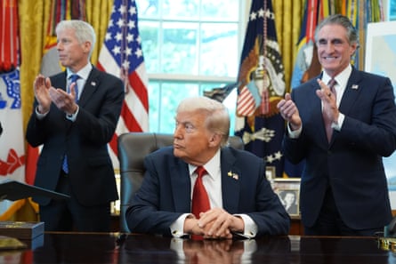 two people clap behind a man seated at a desk